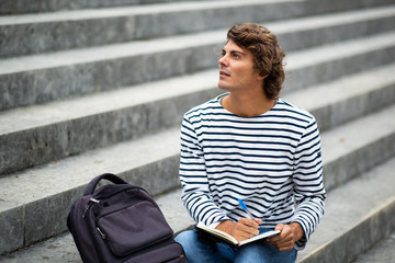 Obraz premium male university student sitting outside writing in book and thinking
