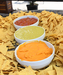 A very large plate or bowl of nachos served with three types of sauce: guacamole,chili and cheese