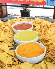 A very large plate or bowl of nachos served with three types of sauce: guacamole,chili and cheese