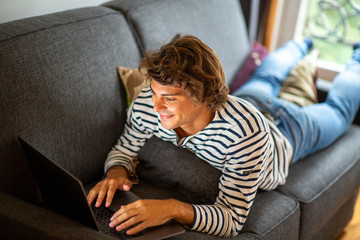 Obraz premium young man relaxing on couch at home using laptop computer