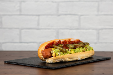 Mexican style hotdog on slate plate and white brick wall 