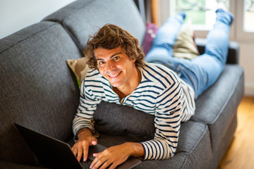 Obraz premium young man relaxing on sofa at home using laptop computer