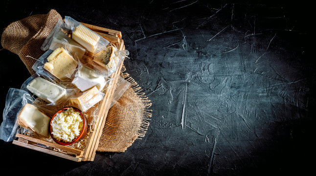 Different varieties of cheese in wooden box. Cheese delicacy on a black concrete background. Top view with copy space