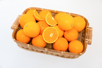 Many oranges in wooden basket and cut orange laying above others isolated on white background. Close-up top view. Citrus fruit and healthy food concept
