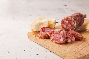 Sliced salami, bread and cutting board on a white background, viewed from the front, with space for text.