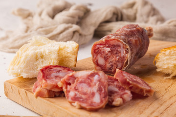 Sliced salami, bread and cutting board on a white background, seen from the front.