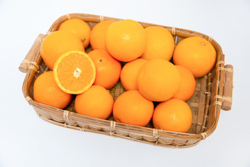 Half of orange laying on many oranges in wooden basket isolated on white background. Close-up top view. Citrus fruit and healthy food concept