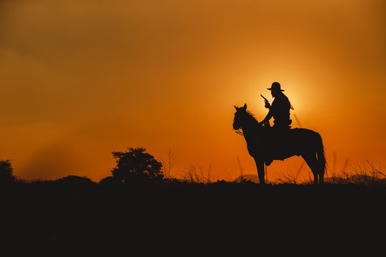 Silhouette the cowboy riding on a mountain with an yellow sky.