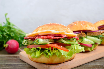 Different burgers on a wooden board. Homemade bun with ham or meat or salami, vegetables, herbs. Sandwiches for lunch.