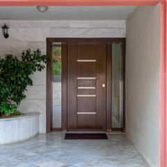 dark pink portico of apartment building entrance covered with white marble, potted plants and dark wood door