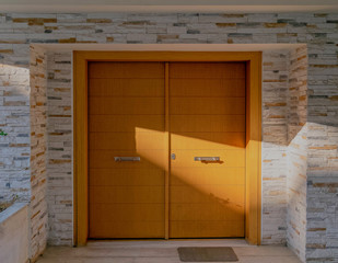 sun rays on contemporary house entrance natural wood double door and stone decorated wall, Athens Greece