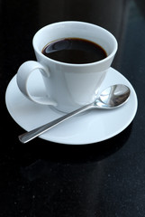 black coffee in a coffee cup  top view with saucers and spoon on a black table.