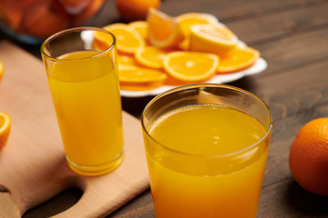Fresh orange fruit whole and sliced on a wooden table, cutting board and kitchen knife. A plate full of citrus slices - natural and healthy food. Glass of fruit cocktail.