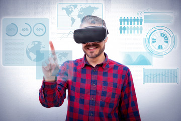 Content man in VR headset pointing at virtual statistics with finger. Front view of cheerful bearded man in checkered shirt using virtual reality headset on grey background. Technology concept