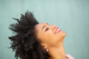 side portrait beautiful young black woman with afro hair laughing against green background