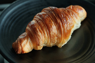 Classic crispy French butter croissant on a black plate. Dark photography 