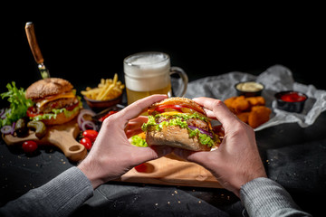 Man holds delicious hamburger in both hands and preparing to bite it on dark background