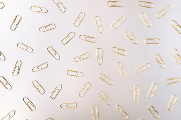 Set of golden paper clips on light silver background. Flat lay. Office and business concept. Backdrop for your design.