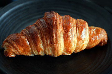 Classic crispy French butter croissant on a black plate. Dark photography