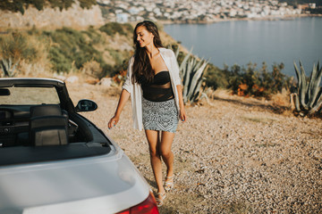 Young woman walking to cabriolet car at seaside