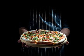Man holding plate with tasty Italian pizza, close up view on a dark background