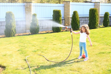 Little girl with a hose in her hands watering a green lawn