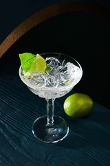 high angle view of cocktail glass with ice, mint leaf and whole lime on blue wooden background
