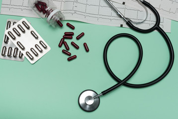 Stethoscope on an EKG with capsules on a green background. Electrocardiogram with black stethoscope