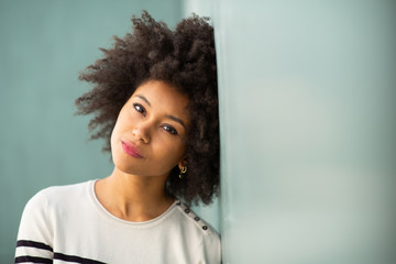 Close up young african american woman with afro hair leaning against wall staring