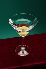 High angle view of crystal cocktail glass with vermouth and whole olive on toothpick isolated on green
