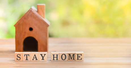 Stay home  message on wooden dices with wooden model house on wooden table and natural...