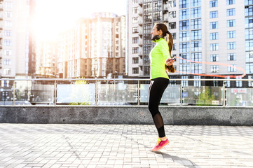 Full leigth girl in sportswear with a headphones jumps with skipping rope on the street. Outdoor...