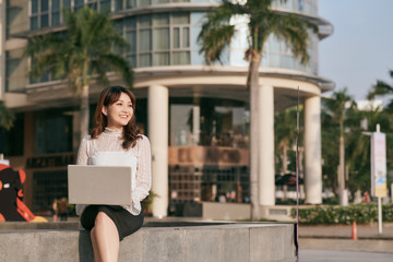 Young woman using laptop computer and smartphone. Beautiful student girl working on laptop outdoor