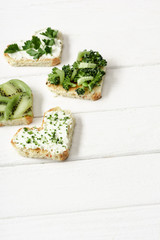 heart shaped canape with creamy cheese, broccoli, microgreen, parsley and kiwi on white wooden surface