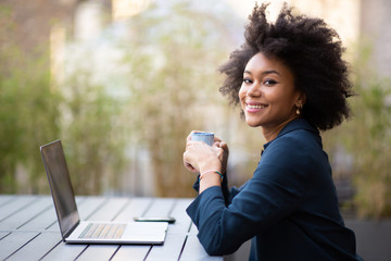 smiling young african american business woman sitting with laptop and cup of coffee