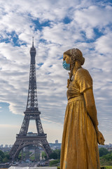 Fototapeta na wymiar Paris, France - 05 06 2020: Golden statue of a woman wearing a surgical mask during confinement against coronavirus and the eiffel tower
