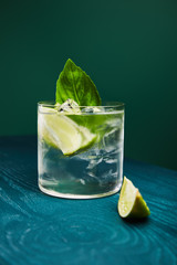 close up view of old fashioned glass with drink and lime on blue wooden surface isolated on green