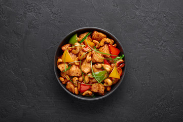 Gai Pad Med Mamuang or Thai Cashew Chicken in black bowl on dark slate backdrop. Kai Med Ma Muang is thai cuisine dish with chicken meat, capsicum, onion, scallions, chilli. Thai Food. Copy space