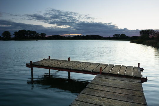 Fishing pier made of boards on the lake and clouds after sunset