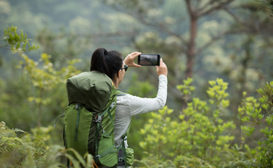 Woman hiker using smartphone taking pictures in spring mountain