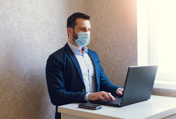 Man in medical mask and jacket is working on laptop.