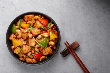 Gai Pad Med Mamuang or Thai Cashew Chicken in black bowl on grey concrete backdrop. Kai Med Ma Muang is thai cuisine dish with chicken meat, capsicum, onion, scallions, chilli. Thai Food. Copy space