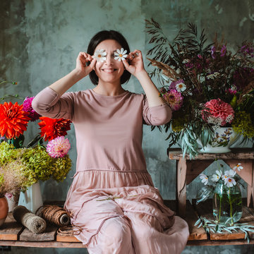 woman professional florist with humor poses with flowers eyes sitting wooden table with compositions wild flowers.