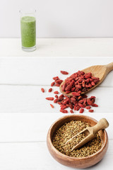 collage of natural fenugreek in wooden bowl with spatula, green smoothie and goji berries on white surface