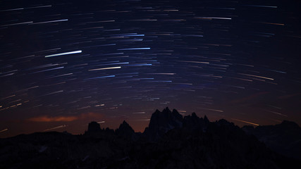 Mountain silhouettes with star trails in the night sky at Three Peaks in the Dolomite Alps , South Tyrol Italy.