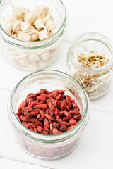 selective focus of goji berries and sprouts in glass jars on white wooden surface