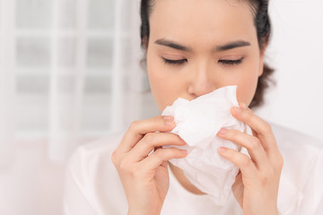 Sick woman covered with a blanket lying in bed with high fever and a flu, blowing her nose.