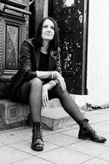 Brunette woman wearing in black leather jacket sitting on stone step. Rock concept. Girl model in the Batumi, Georgia. Old door at the background. Black and white.