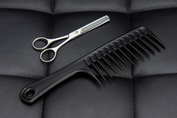 Hairdresser tools. Scissors and comb on a leather background