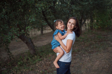 Fototapeta premium Young mother and happy daughter. A stylish family in an apple garden in the fall.